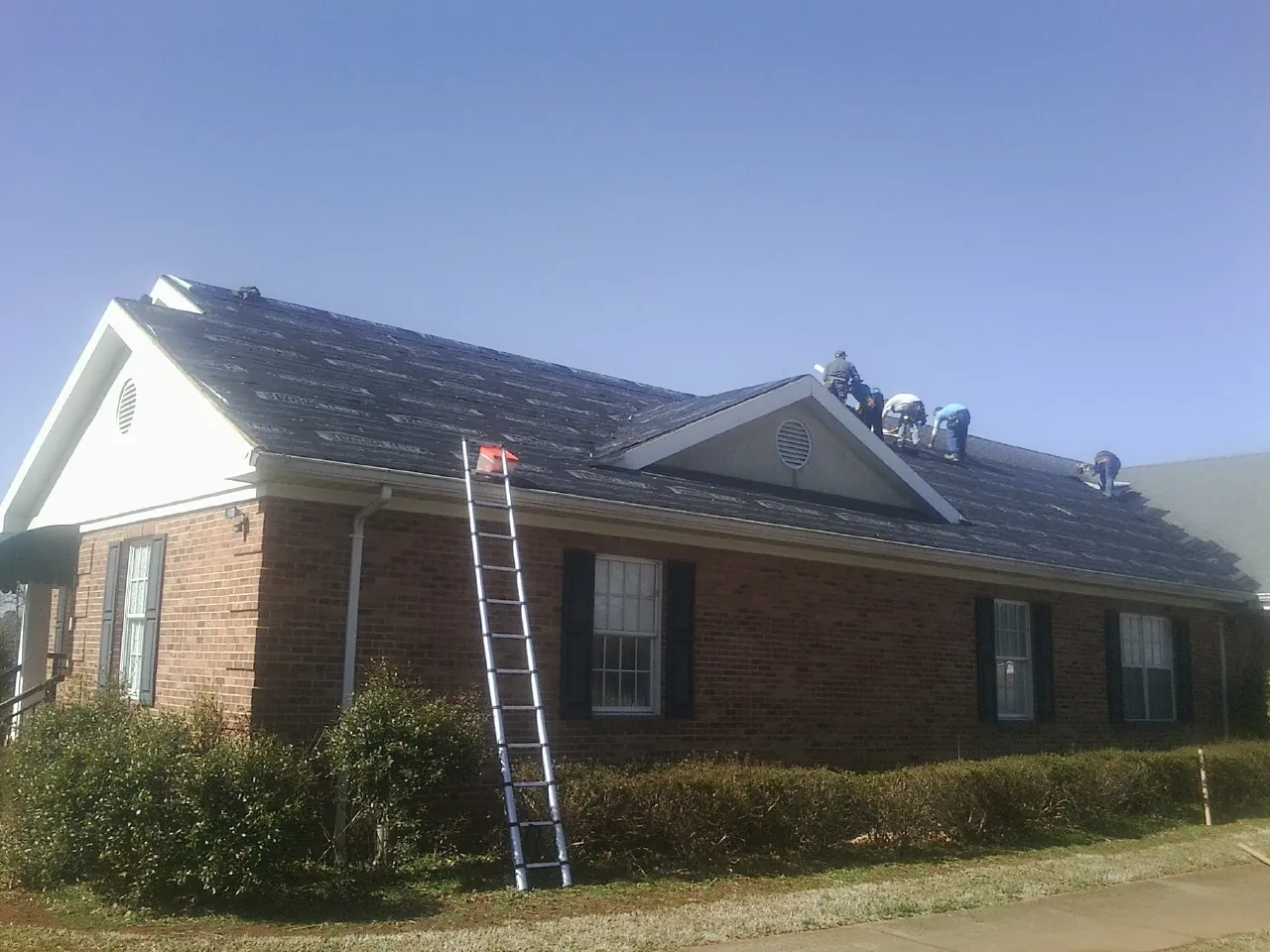 Crew tearing shingles off a brick ranch roof with a ladder set — Emergency Roof Repair work by our crew in Meeker
