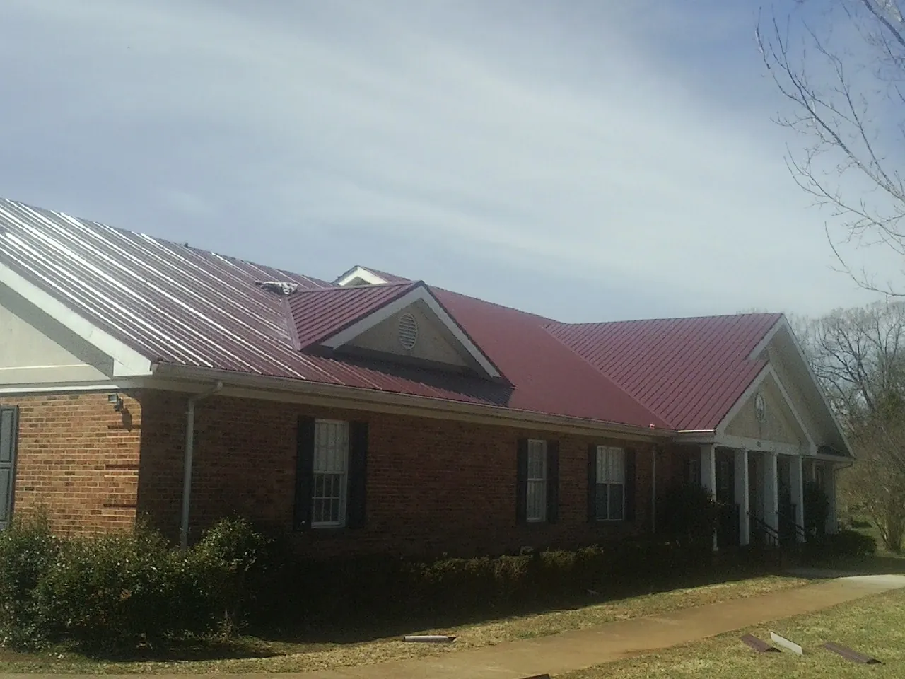 Red metal roof with gabled entries on a long brick building, from a Hail Damage Roof Repair job in Meeker