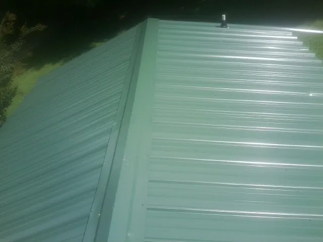 New green metal panels meeting at the ridge of a roof — Flat Roof Repair work by our crew in Meeker