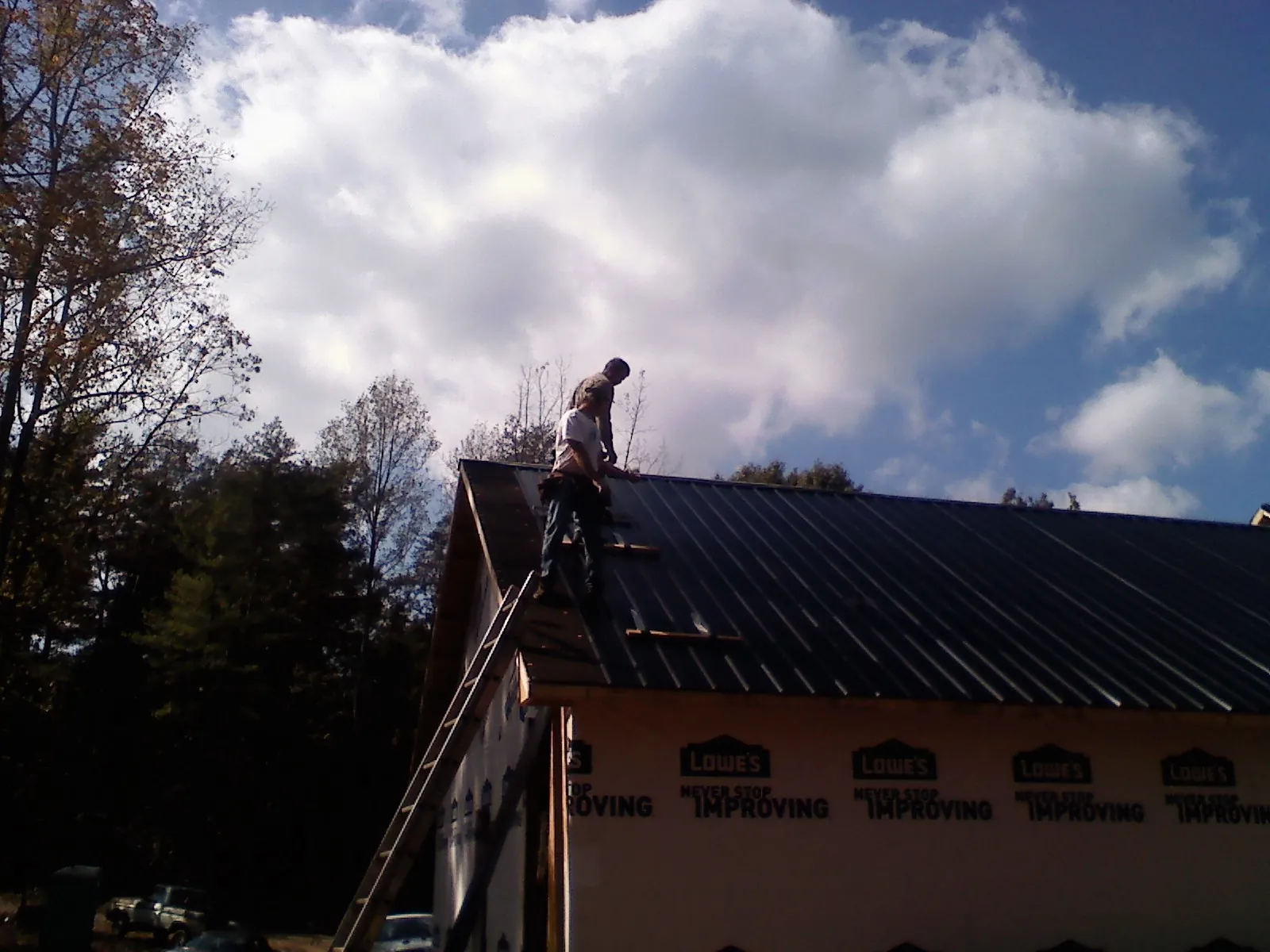 Roofer fastening dark metal panels high against a cloudy sky in Meeker