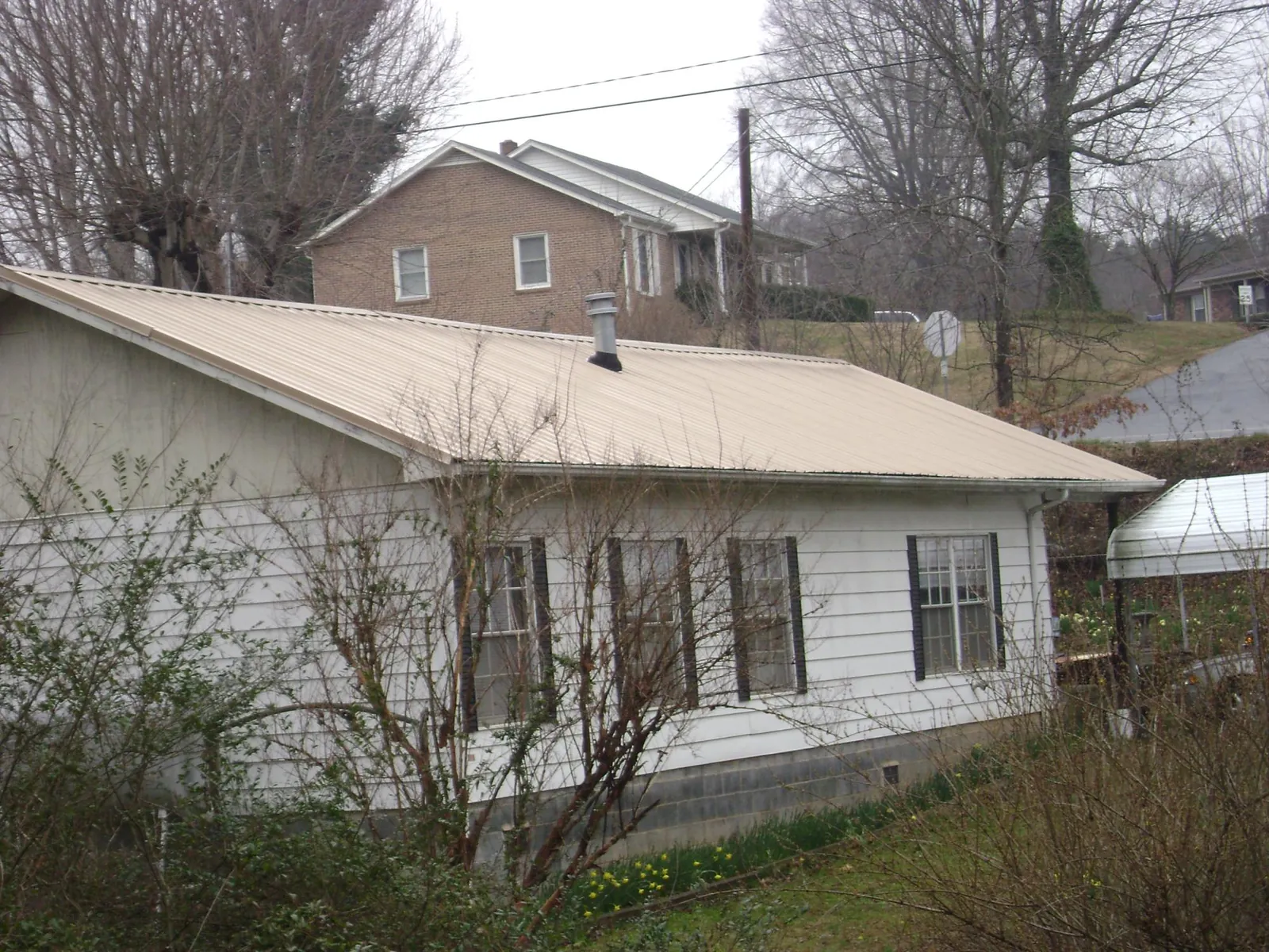 Tan metal roof on a white sided house set into a hillside — Commercial Roofing by Roofing Brothers in Meeker